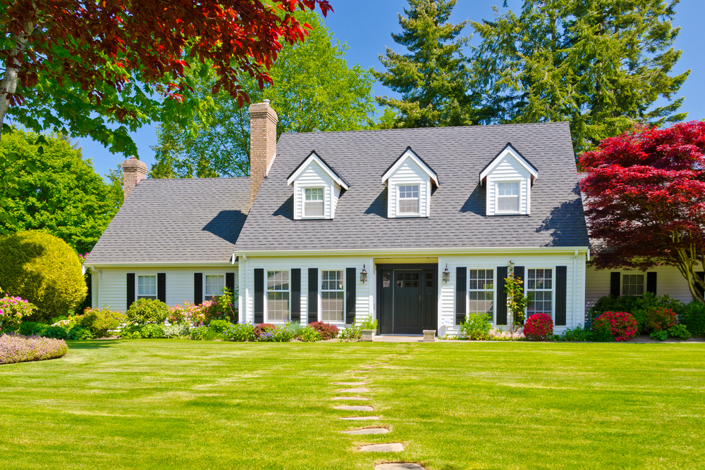 A cape cod home with 3 dormers, white, with a nice lawn