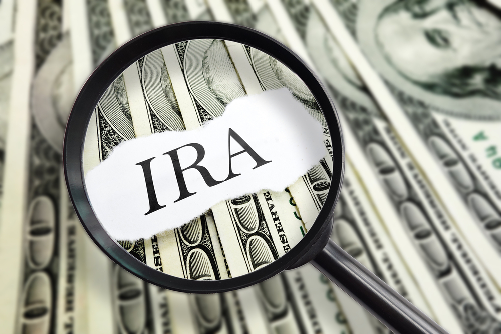 The word IRA with a magnifying lense over it and $100 dollar bills in background