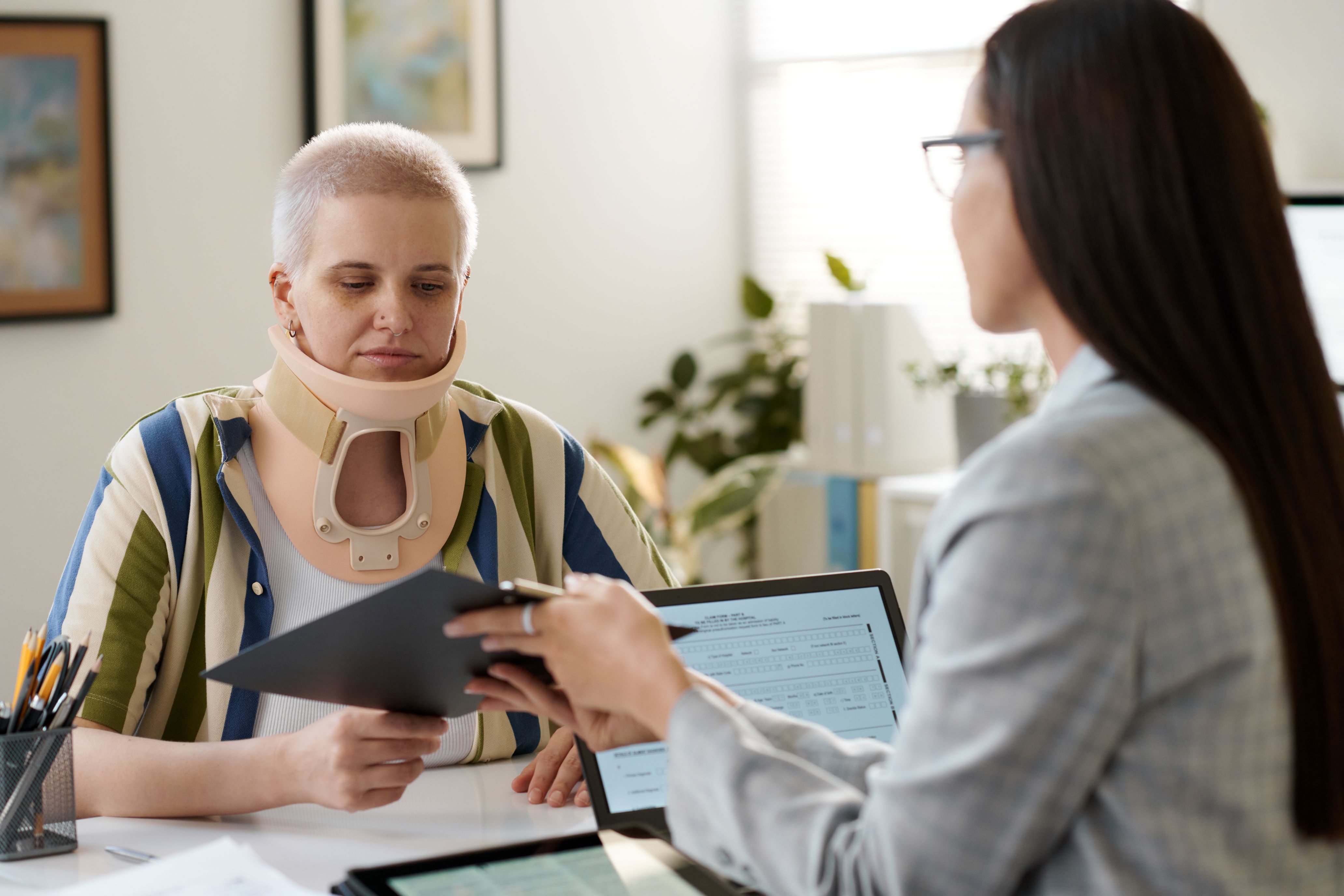 Woman wears neck brace and examines paperwork with disability attorney.