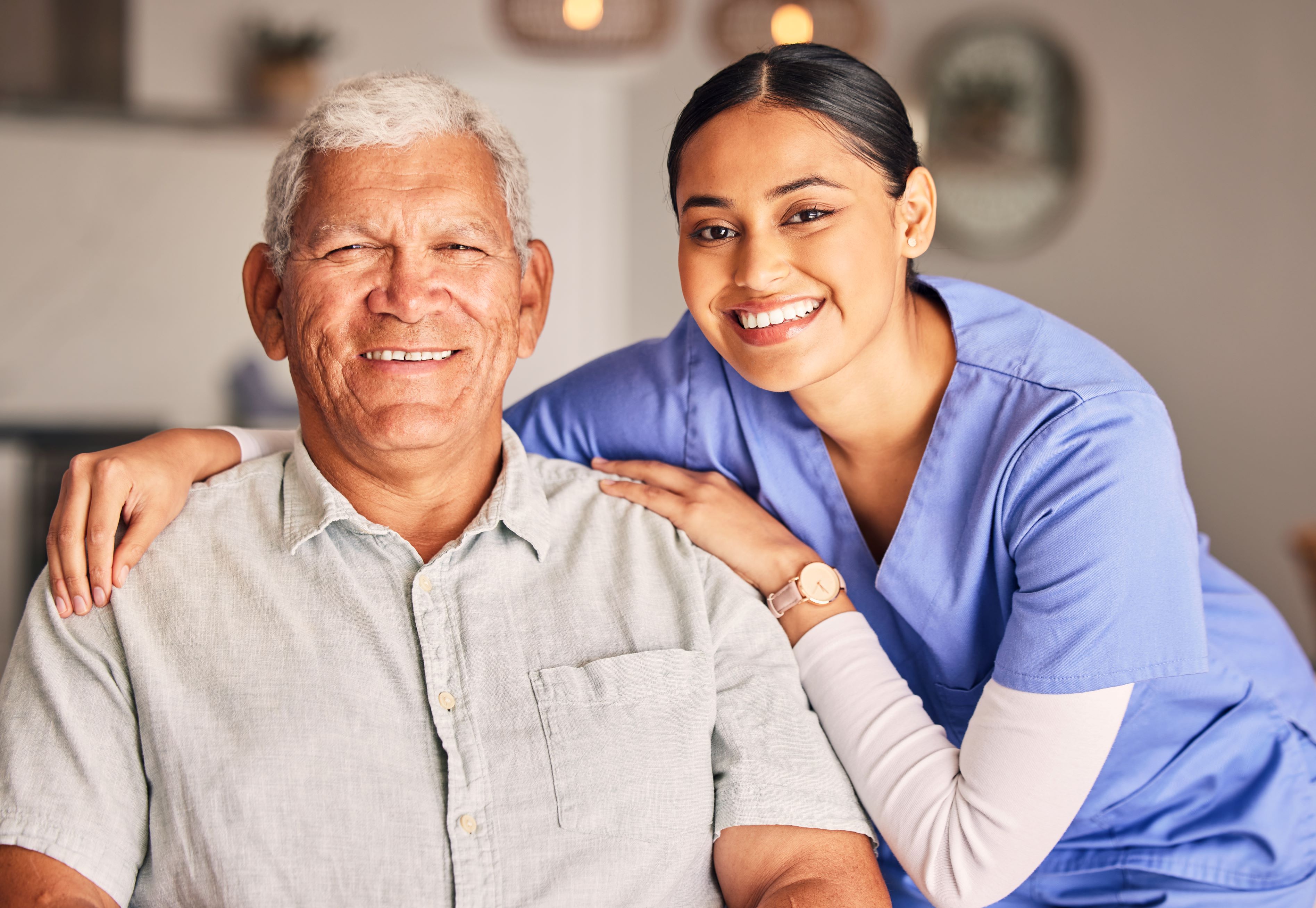 Health care provider at nursing home poses holding shoulders of smiling senior resident..