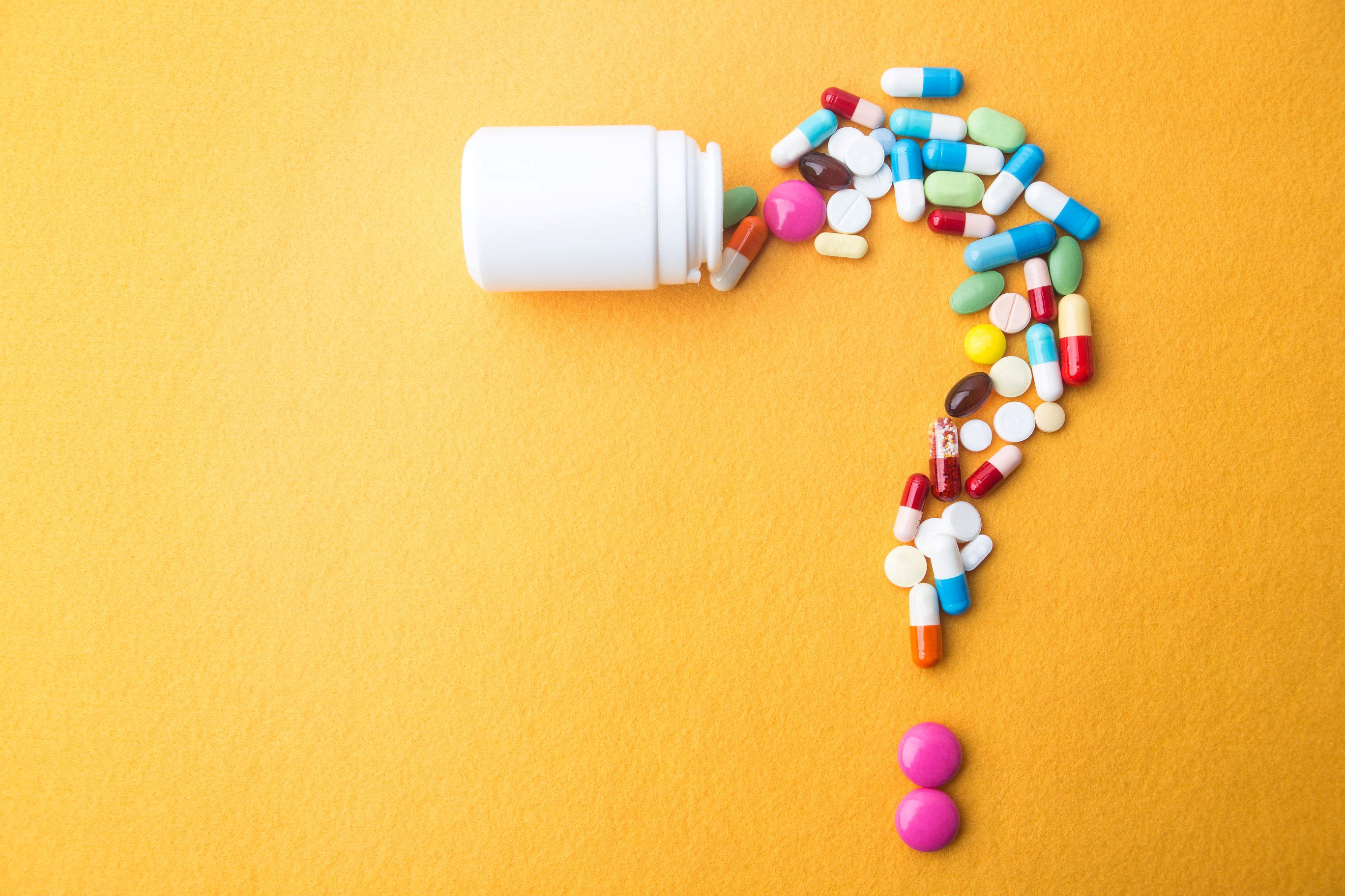Prescription pills spilling out of white plastic bottle into shape of a question mark.