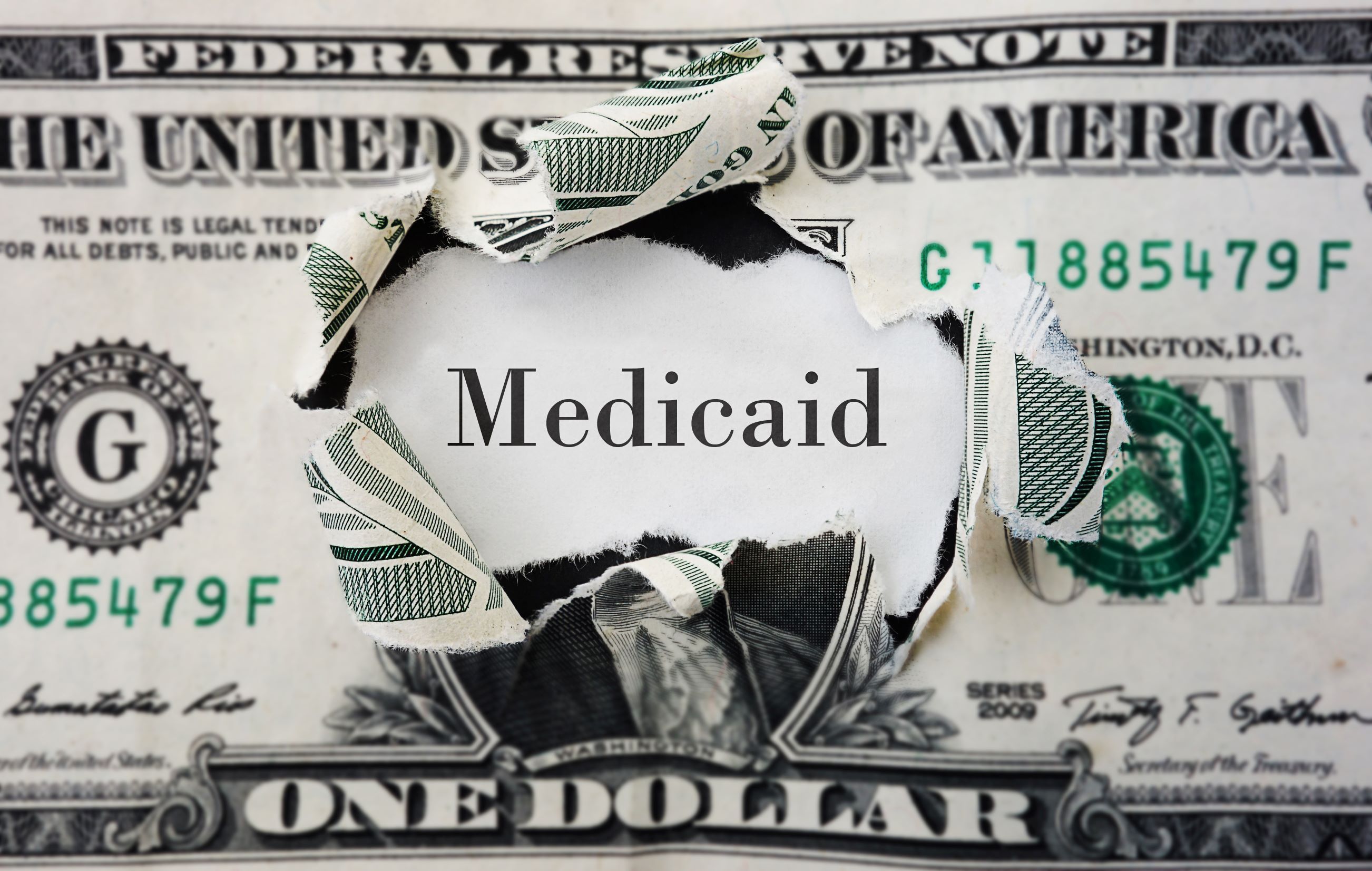 Dollar bill ripped open to reveal the word Medicaid.