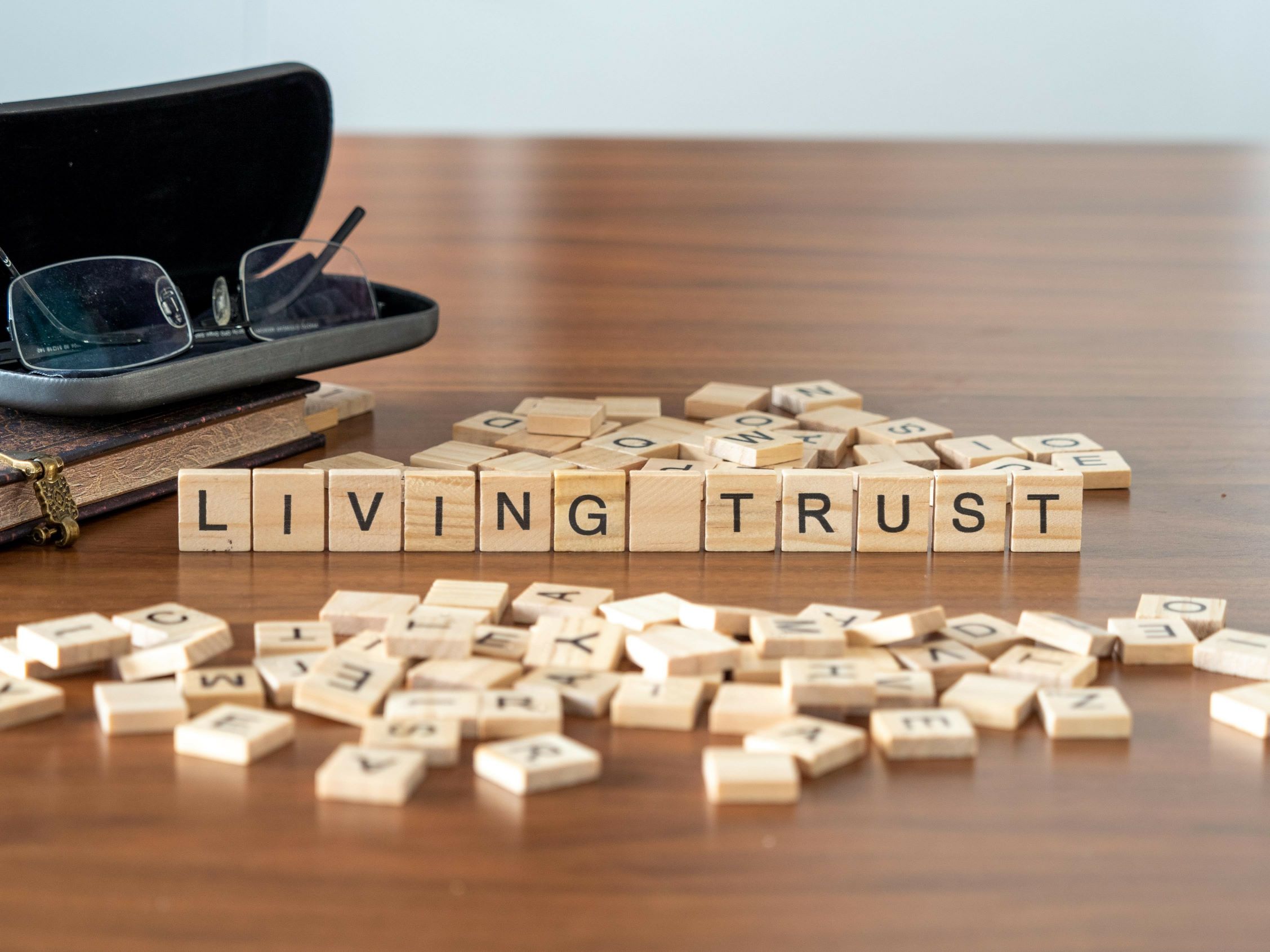 Wooden tiles spell out Living Trust on a tabletop alongside eyeglasses.