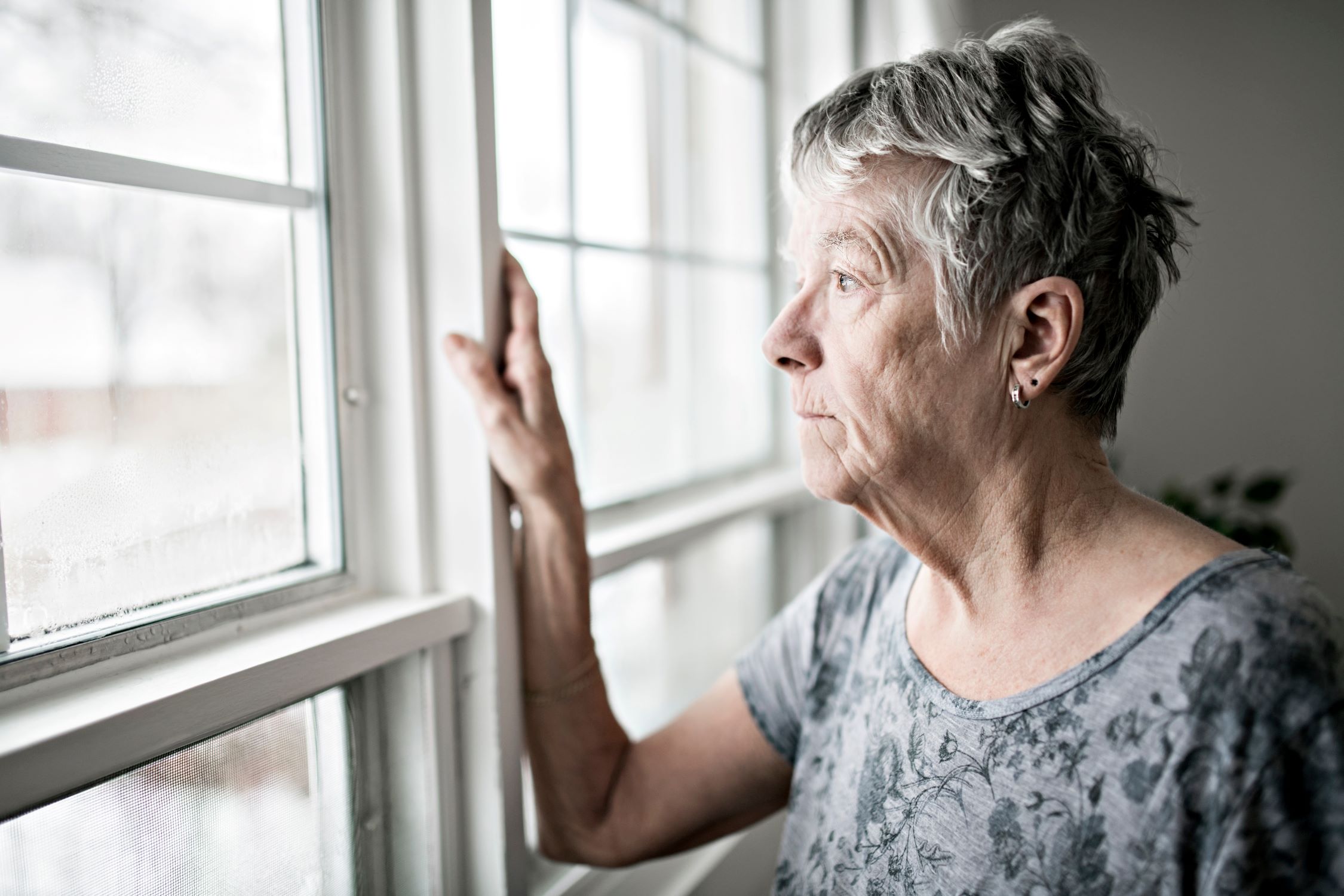 Senior woman, alone, looks out window.