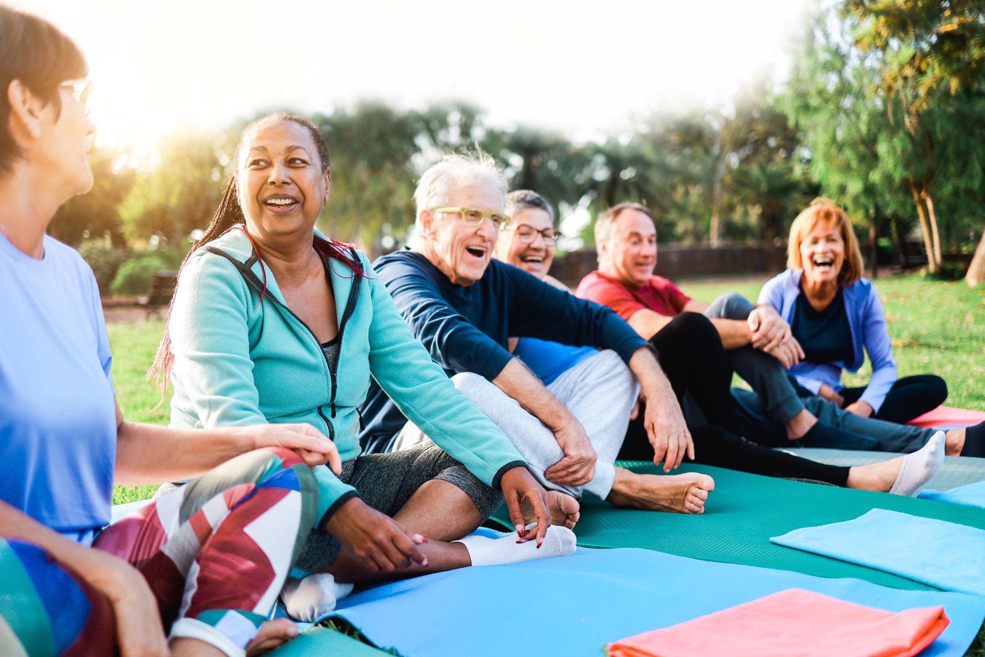 Group of seniors at park smiling and talking after outdoor yoga class.