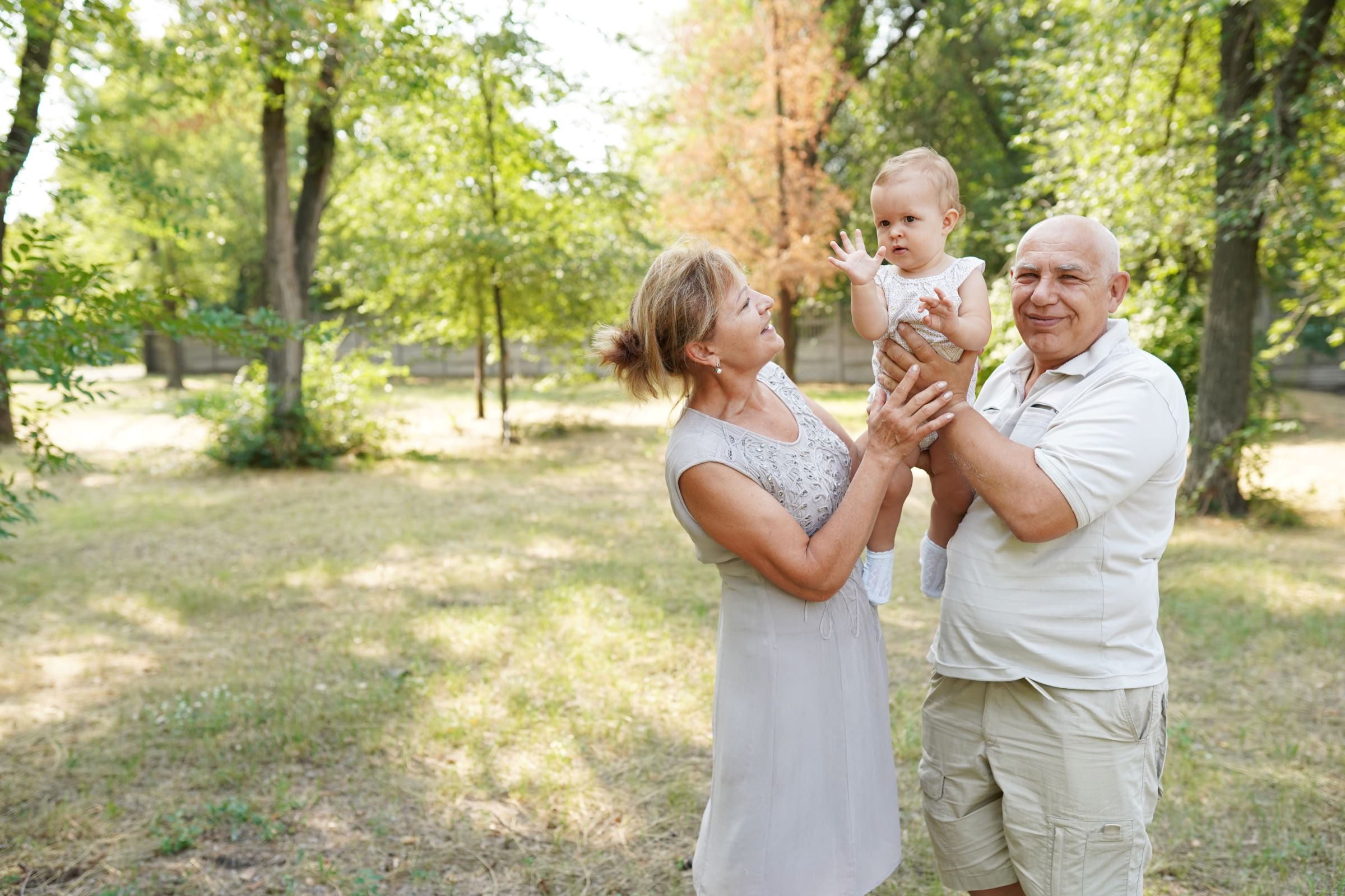 Grandparents stand outside in a park for a photo shoot holding up their new grandchild.